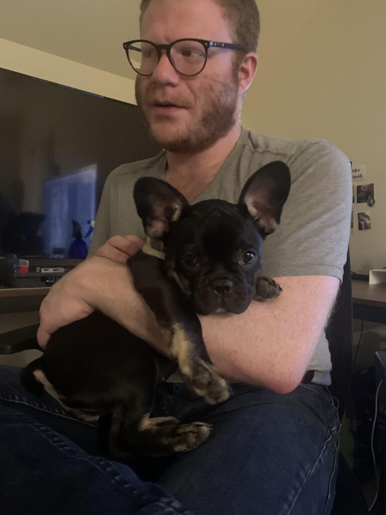 a man with a lens siting down with a french bulldog on his arms